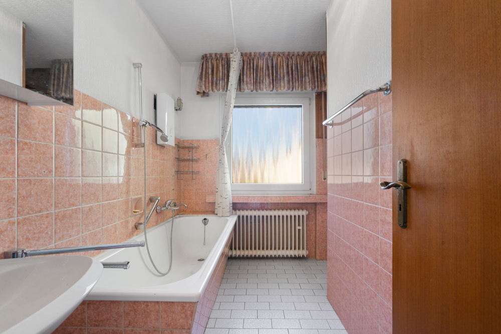 Badezimmer mit Badewanne, Waschbecken und rosa Fliesen, Fenster mit Vorhang.