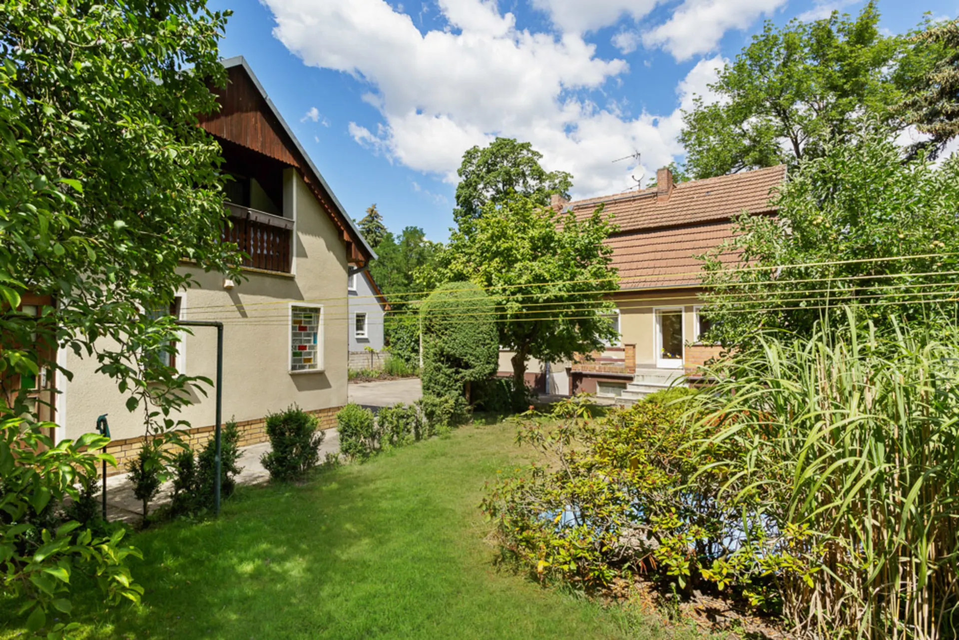 Zwei Wohnhäuser mit Garten, Bäumen, Wäscheleinen und Sträuchern bei sonnigem Wetter.