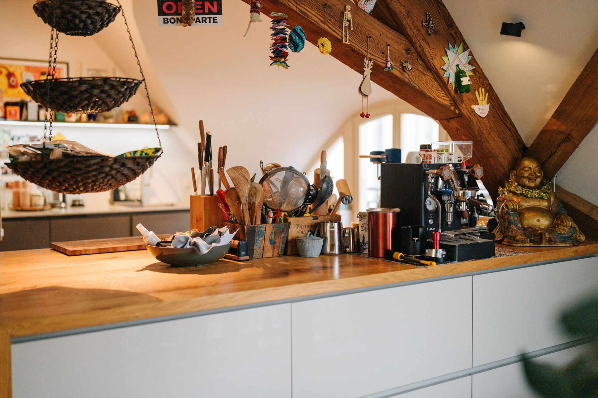 Kücheninsel mit Holzplatte, Küchenutensilien, Espressomaschine und Dekorationen unter Dachbalken.
