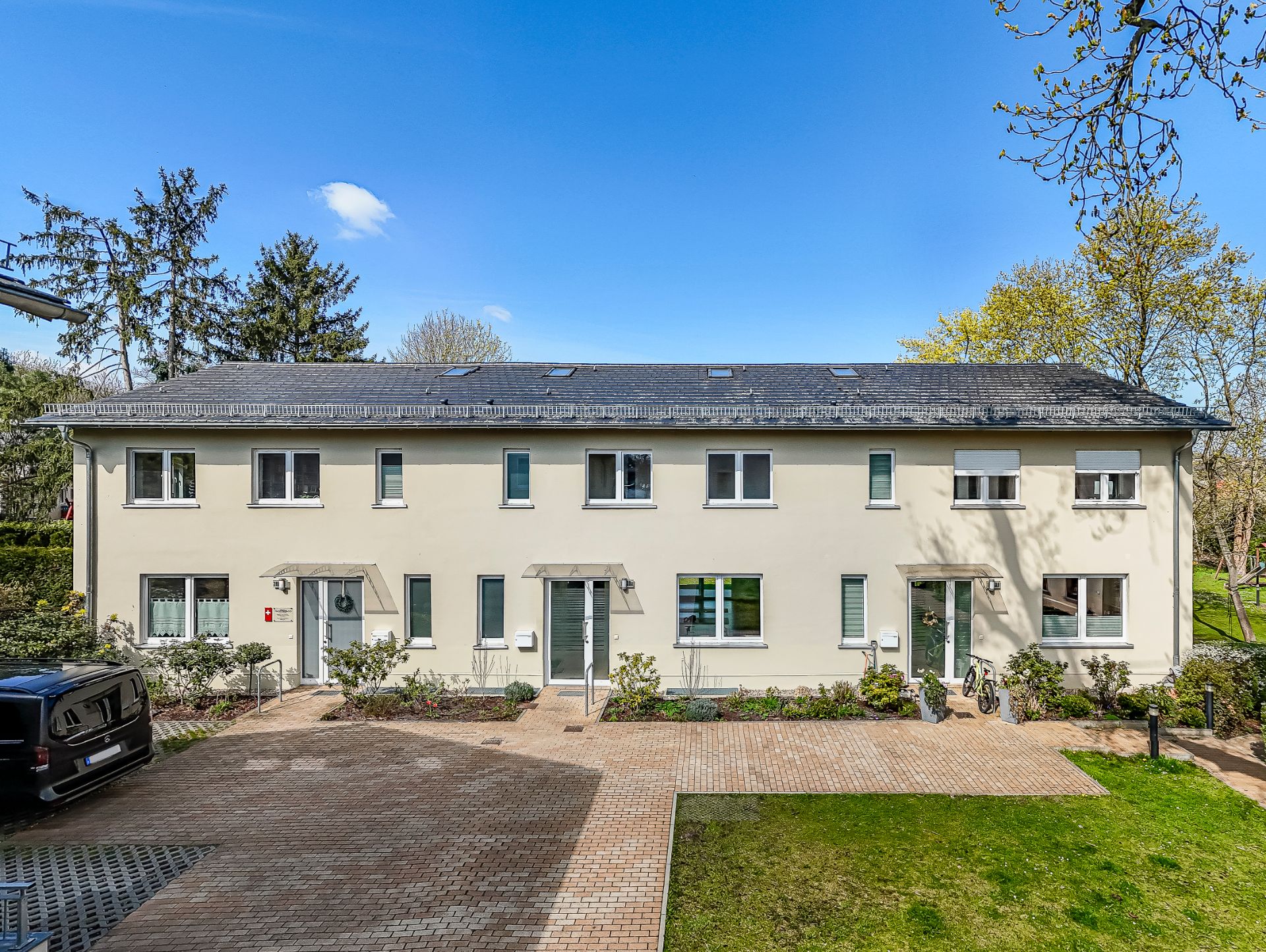 Modernes, zweistöckiges Wohnhaus mit mehreren Eingängen und gepflegtem Vorplatz.