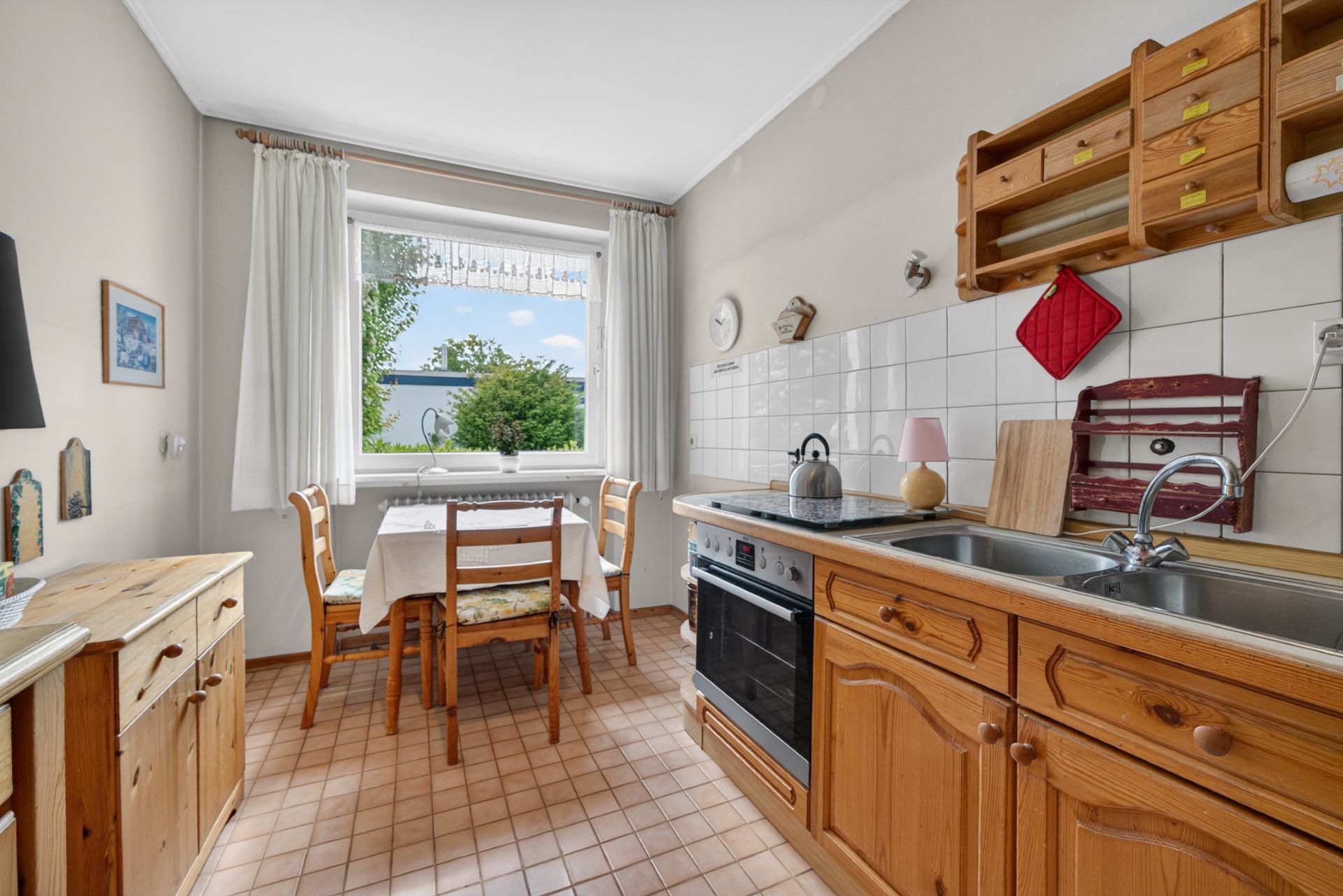 Helle Küche mit Holzmöbeln, Esstisch am Fenster, Herd und Spüle.