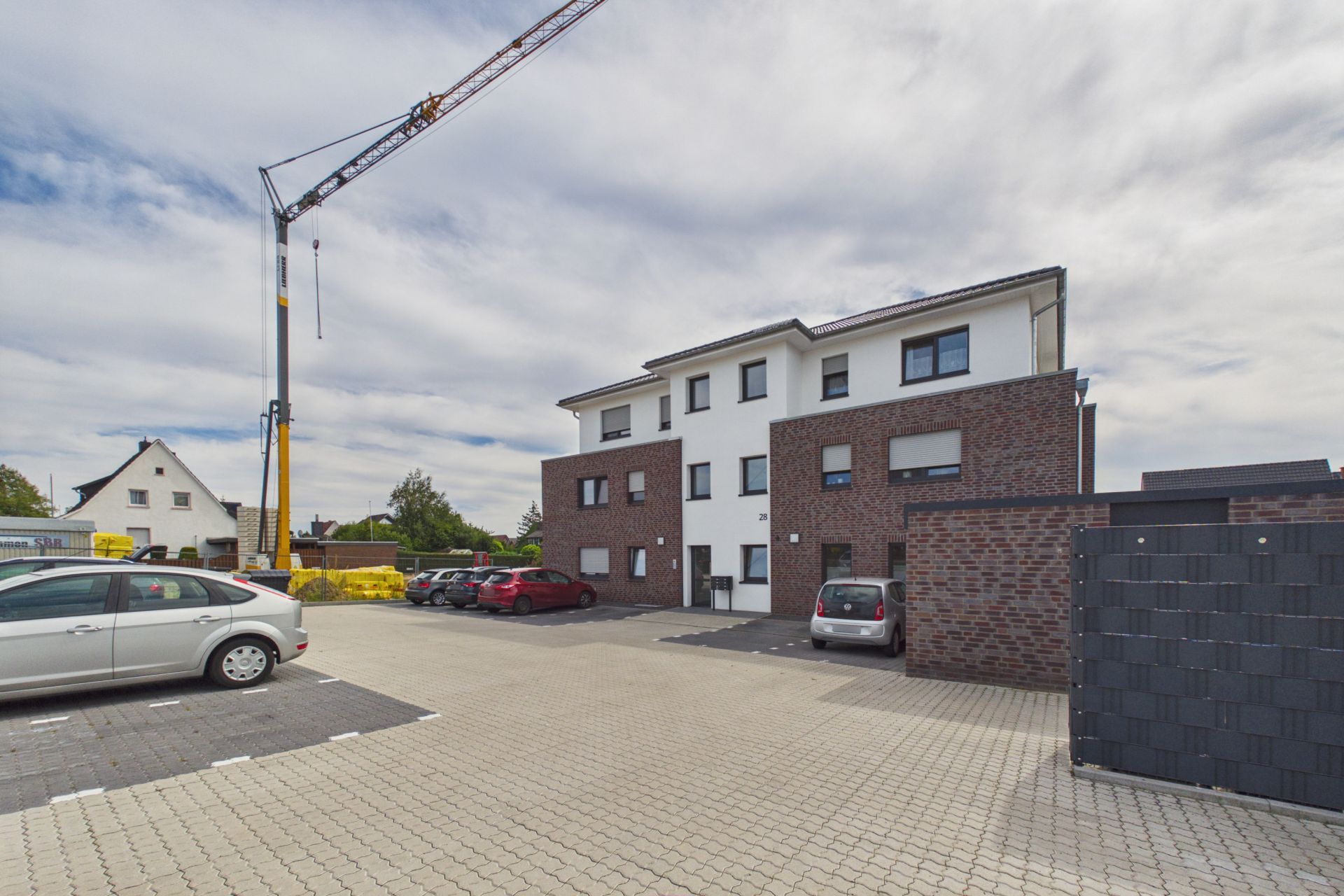 Modernes Wohnhaus mit Ziegelfassade, geparkte Autos und Baukran im Hintergrund.