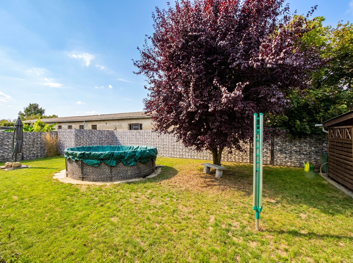 Garten mit rundem Pool mit Abdeckung, Baum, Wäscheständer und Rasenfläche.