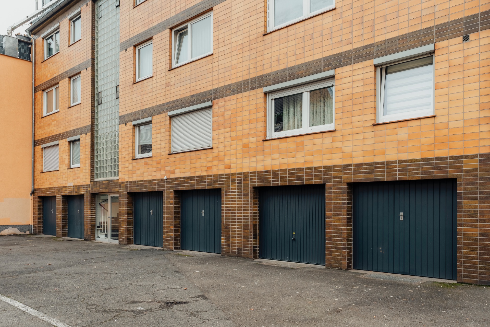 Mehrfamilienhaus mit fünf geschlossenen Garagentoren im Erdgeschoss.