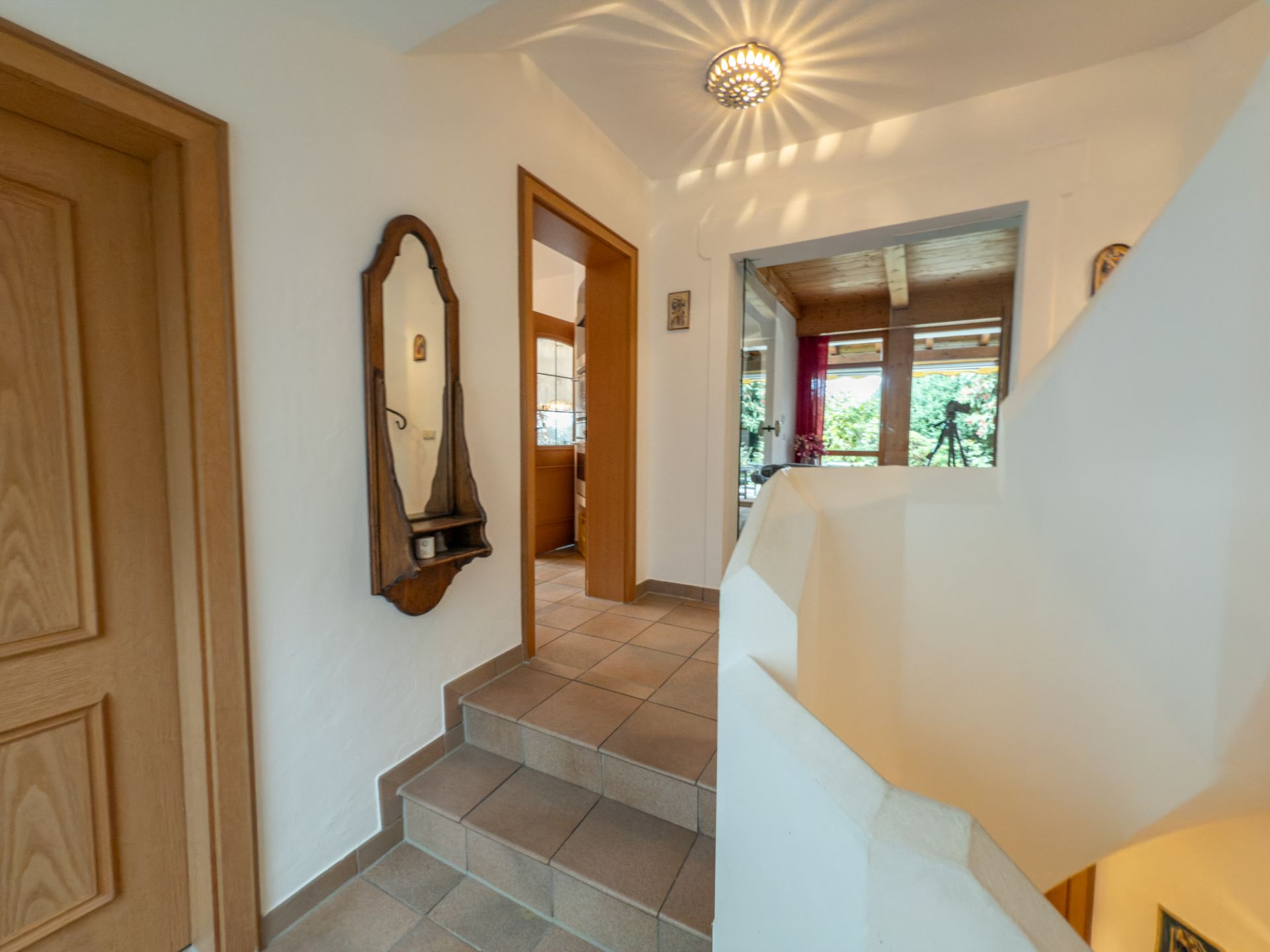 Heller Flur mit Treppe, Holzspiegel und Zugang zu mehreren Zimmern.