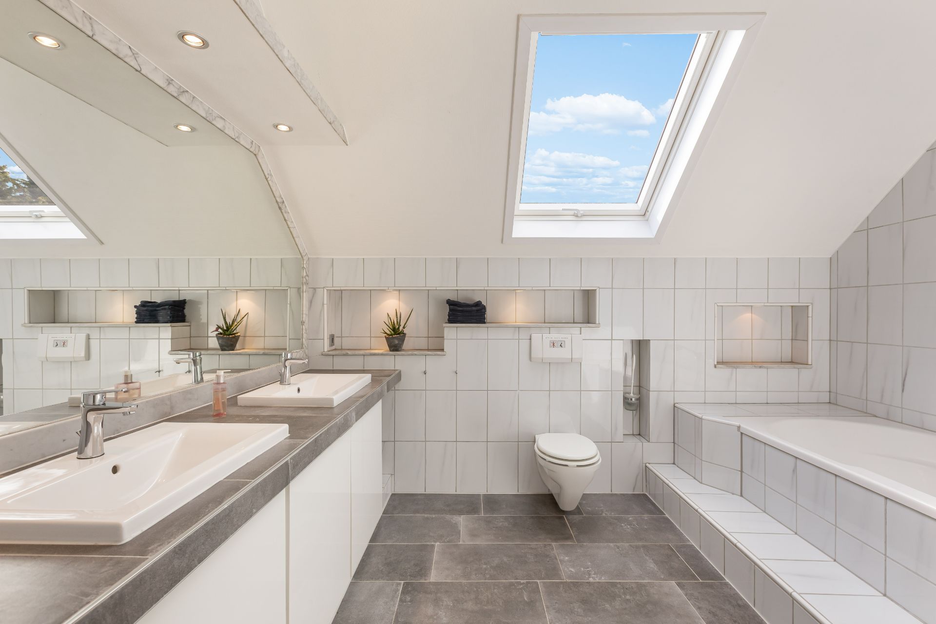 Modernes Badezimmer mit Dachfenster, zwei Waschbecken, Toilette und Badewanne.