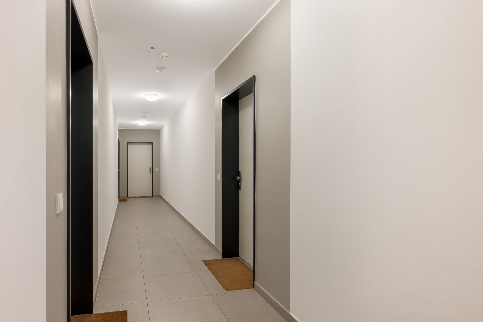 Heller Flur in einem Wohnhaus mit mehreren Wohnungstüren und Fußmatten.