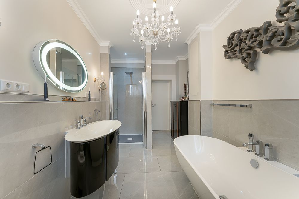 Modernes Badezimmer mit freistehender Badewanne, großem Spiegel, Dusche und Kronleuchter.