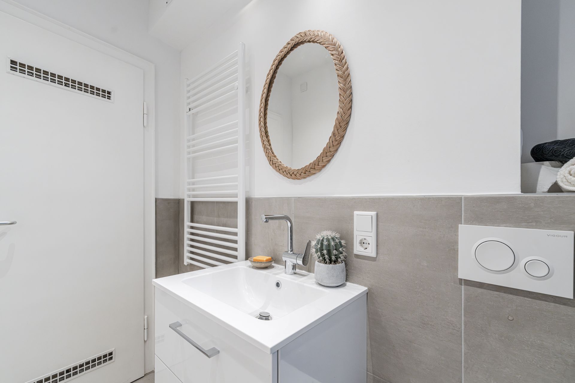 Modernes Badezimmer mit rundem Spiegel, Waschbecken und Handtuchheizkörper.