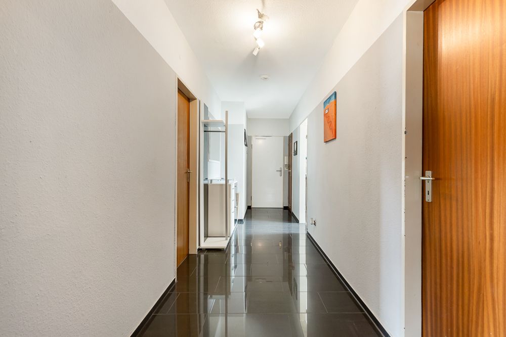 Heller Flur mit glänzendem, dunklem Boden, weißen Wänden und mehreren Holztüren.