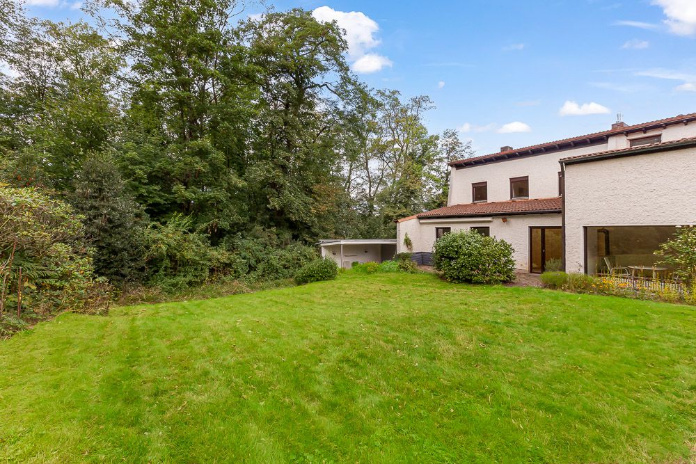 Haus mit großem Garten und Bäumen im Hintergrund.