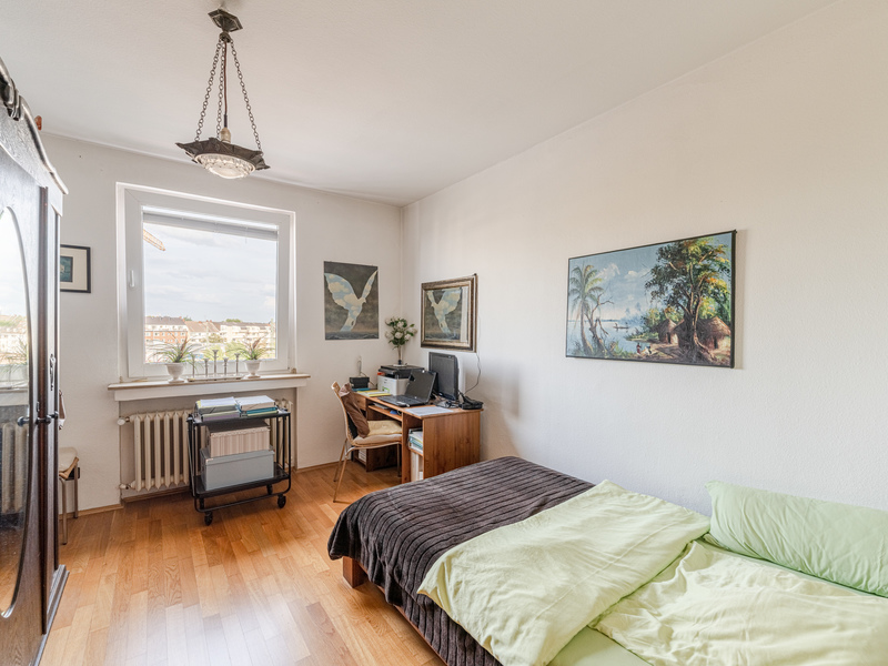 Helles Schlafzimmer mit Bett, Schreibtisch, Stuhl, Fenster und Wandbildern.