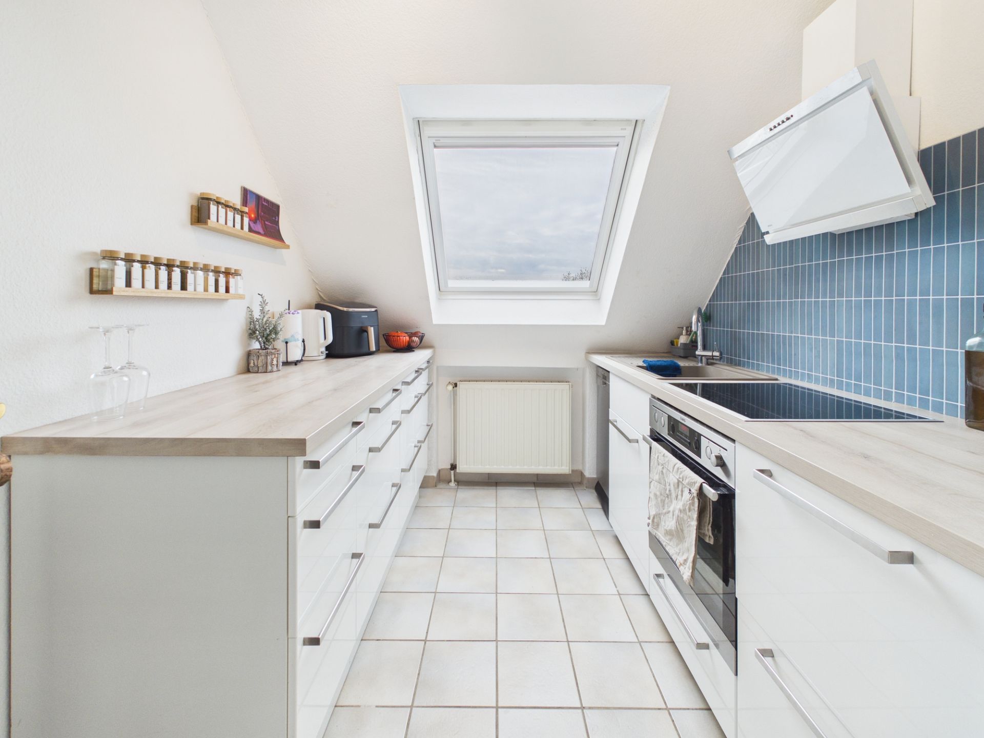 Helle, moderne Küche mit weißen Schränken, blauer Fliesenwand und Dachfenster.