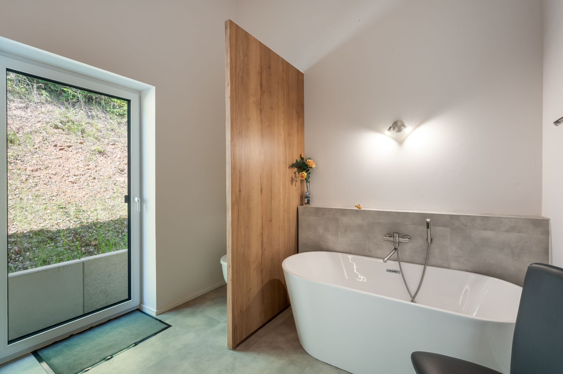 Modernes Badezimmer mit freistehender Badewanne, großer Glastür und Holzwand als Abtrennung.