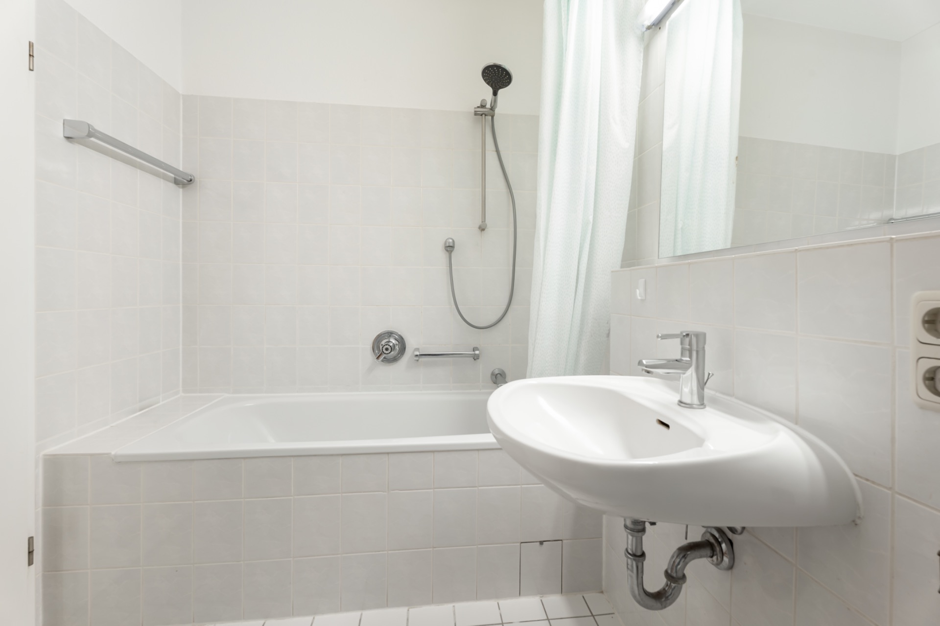 Helles Badezimmer mit Badewanne, Duschbrause, Waschbecken und Fliesen.