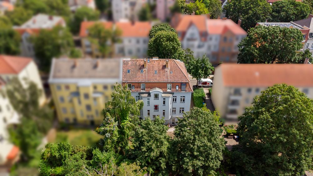 Luftaufnahme eines mehrstöckigen Wohnhauses mit rotem Dach und umliegenden Bäumen.