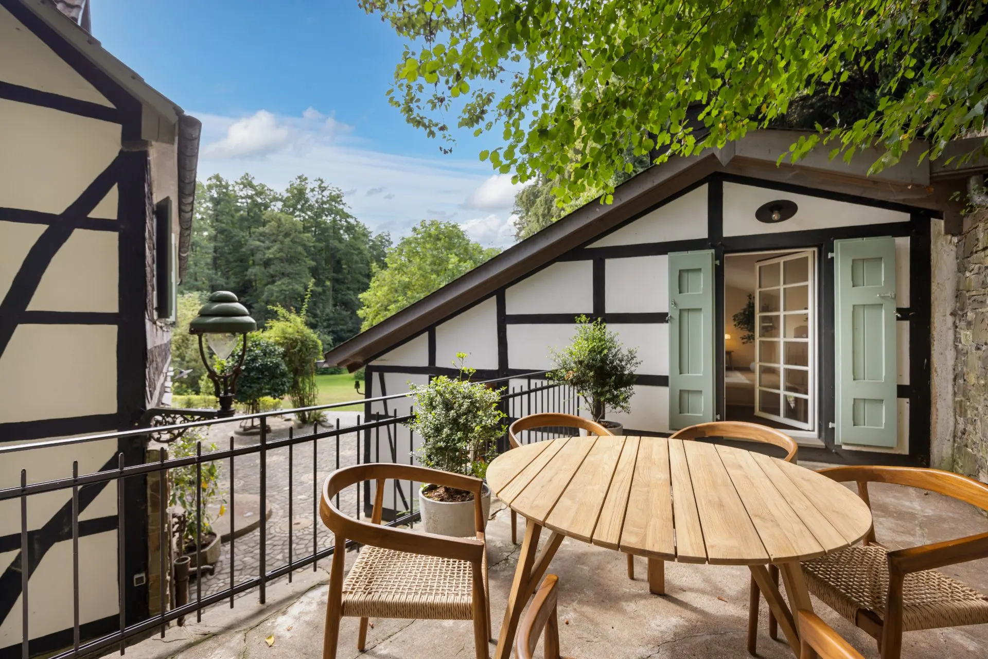 Terrasse mit rundem Holztisch, vier Stühlen und Fachwerkhaus im Hintergrund.