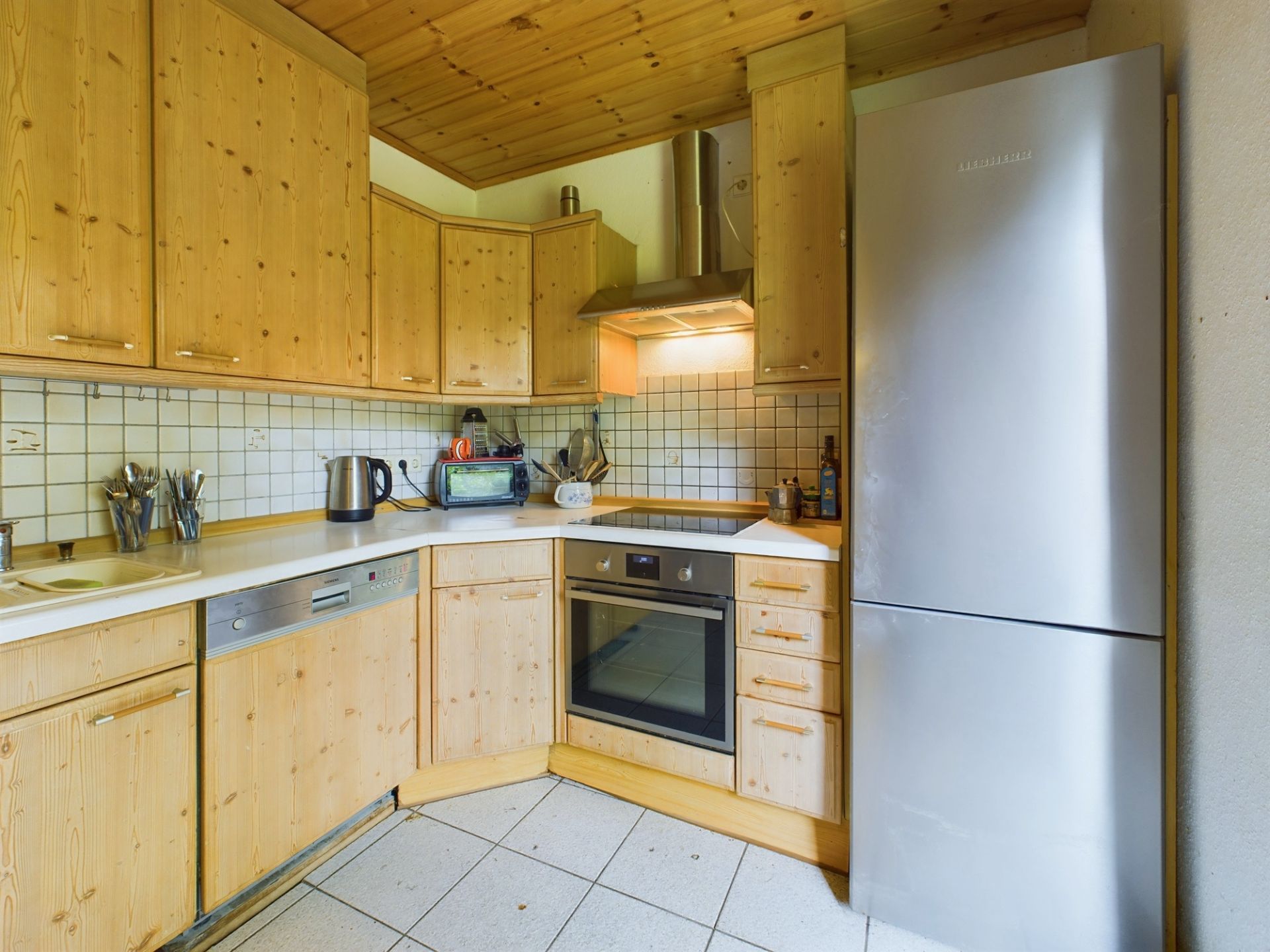 Küche mit Holzschränken, Edelstahl-Kühlschrank, Herd, Backofen und weißen Fliesen.