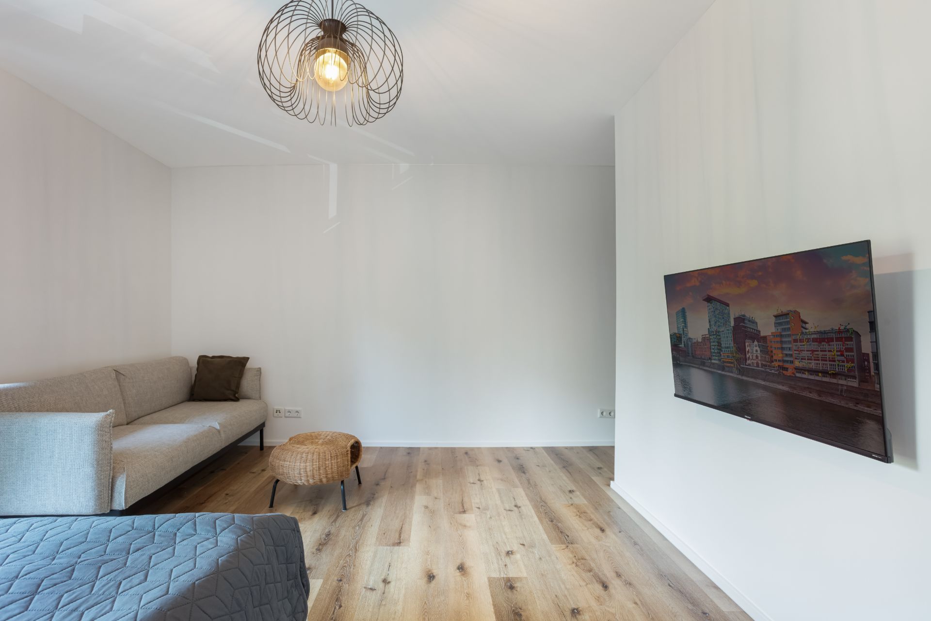 Helles Wohnzimmer mit Sofa, kleinem Tisch, Wandfernseher und Holzfußboden.