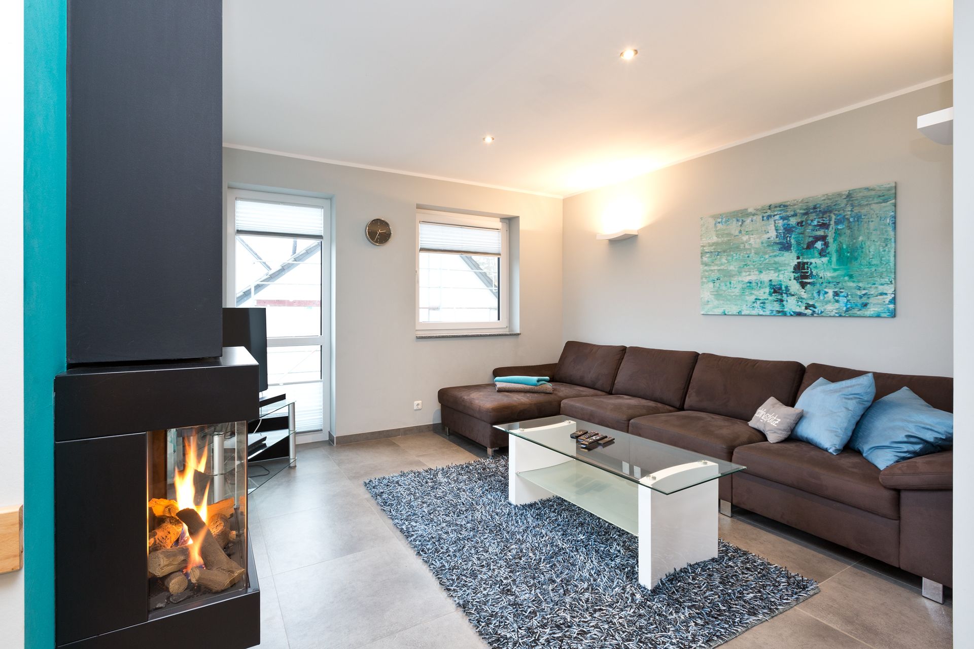 Modernes Wohnzimmer mit braunem Sofa, Kamin, Glastisch und blauem Teppich.