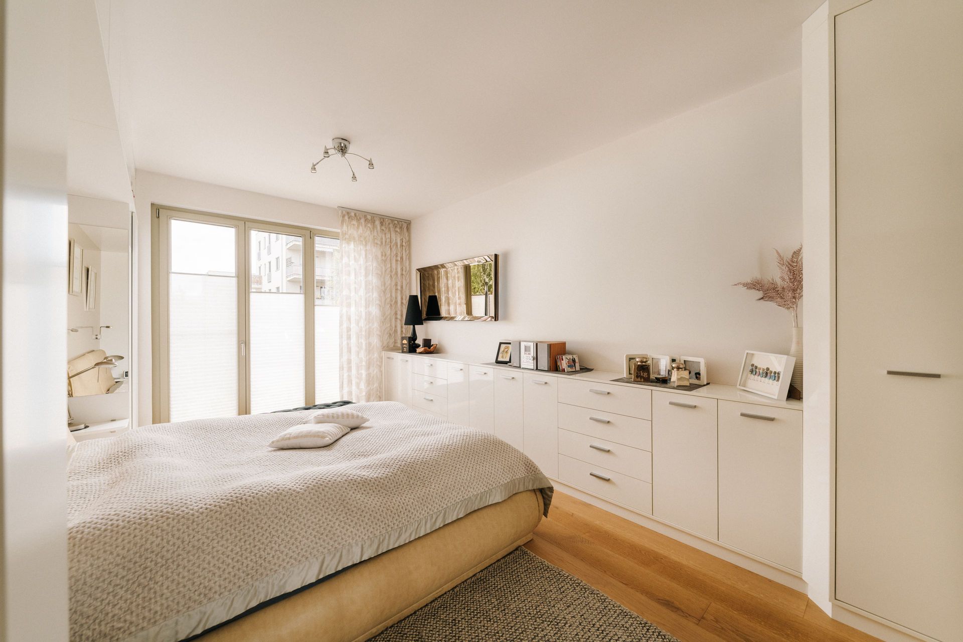 Helles Schlafzimmer mit Bett, weißen Möbeln, Holzboden und großem Fenster.