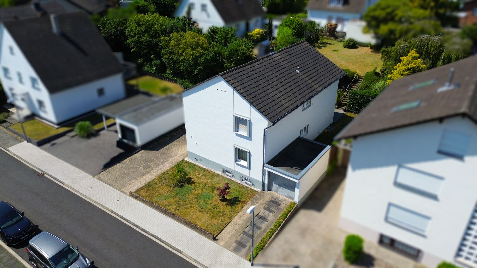 Zweistöckiges, weißes Wohnhaus mit Garage, kleinem Vorgarten und gepflasterter Einfahrt in einer Wohnsiedlung.