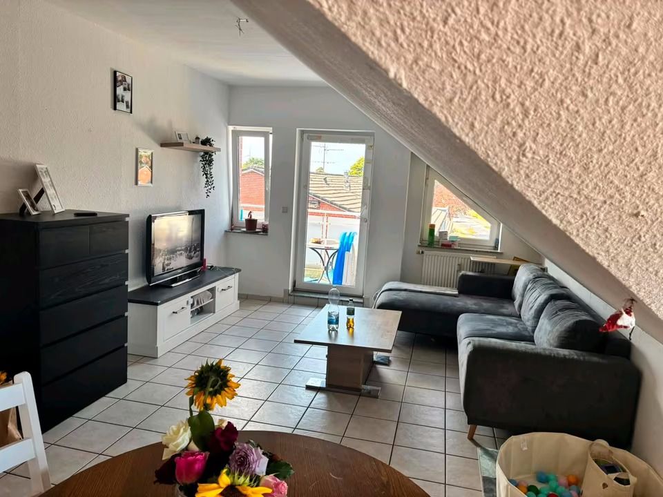 Wohnzimmer mit grauem Ecksofa, TV, Couchtisch und Blumen auf einem Esstisch, helle Fliesen.