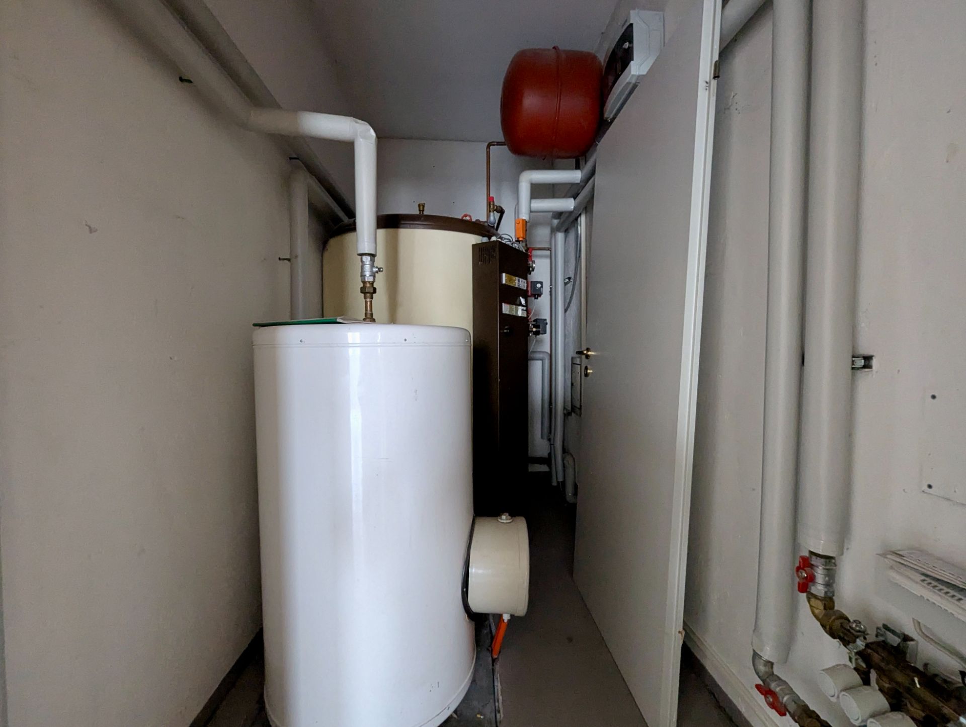 Ein schmaler Hauswirtschaftsraum mit Heizungsanlage, Rohren und einem weißen Boiler.