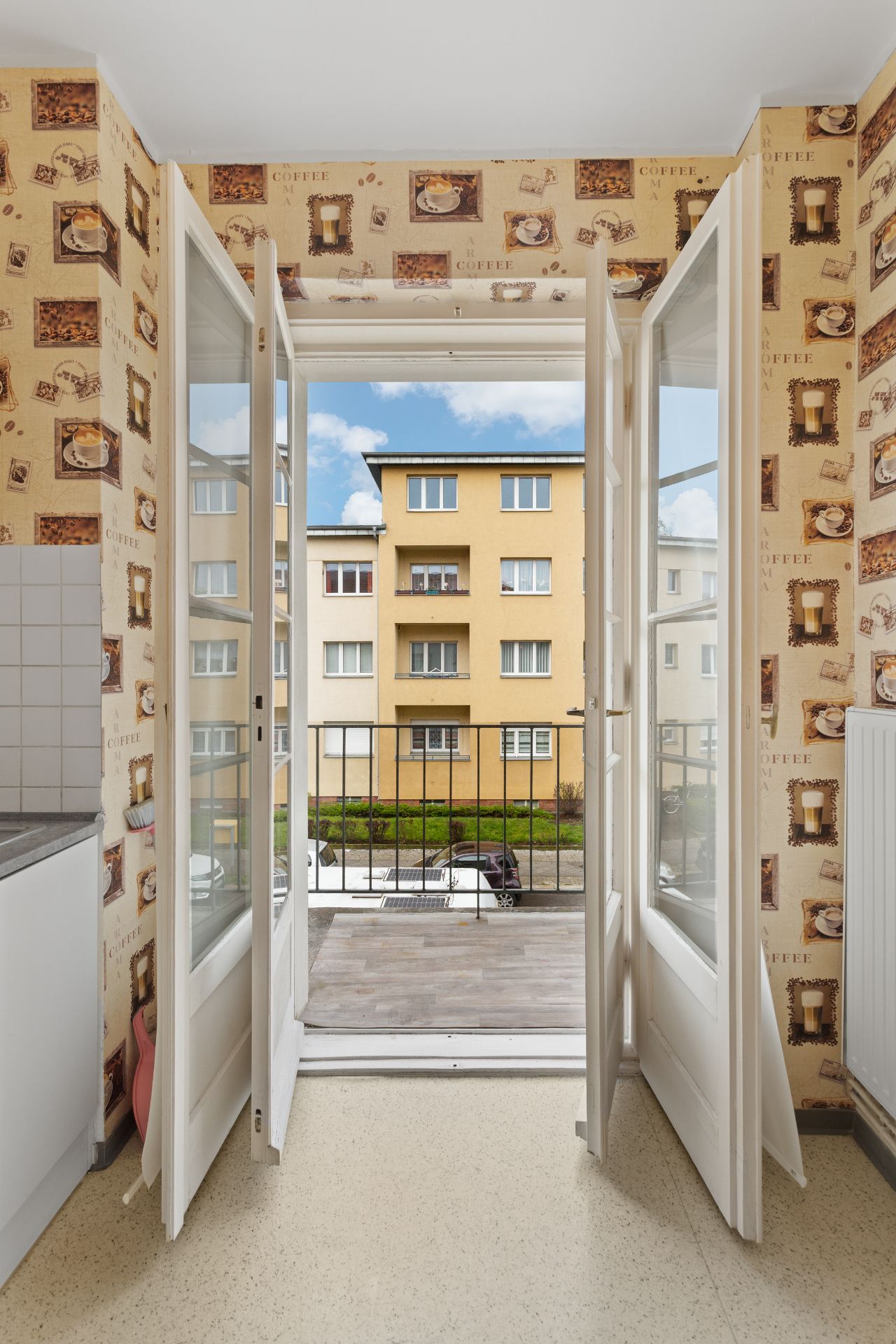 Blick aus einer Küche mit offener Balkontür auf einen Balkon und ein gelbes Wohnhaus.