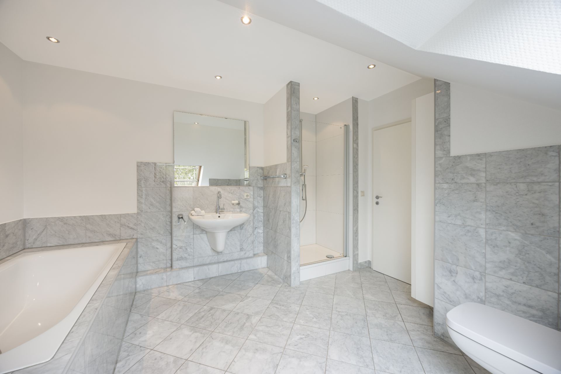 Helles Badezimmer mit Badewanne, Dusche, Waschbecken, Spiegel und WC, Fliesenboden und Wandfliesen.