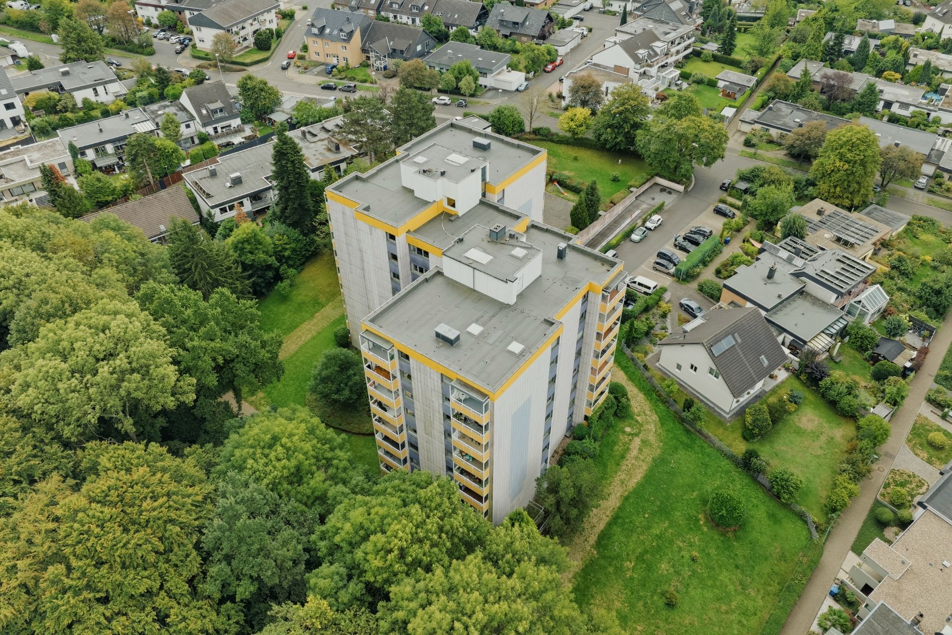 Luftaufnahme eines mehrstöckigen Wohnhauses mit umliegenden Bäumen und Nachbarhäusern.