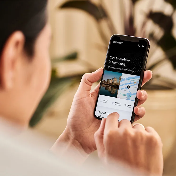 Person hält ein Smartphone mit Immobilienanzeige für Hamburg in der Hand.