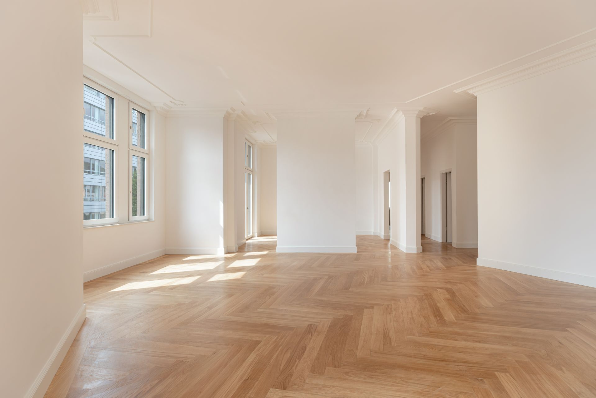 Heller leerer Raum mit großen Fenstern und Parkettboden.