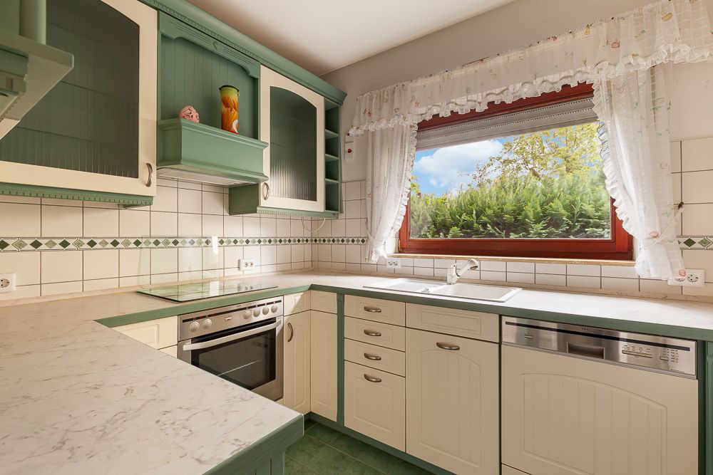 Helle Küche mit grünen und weißen Schränken, großem Fenster und Marmortheke.