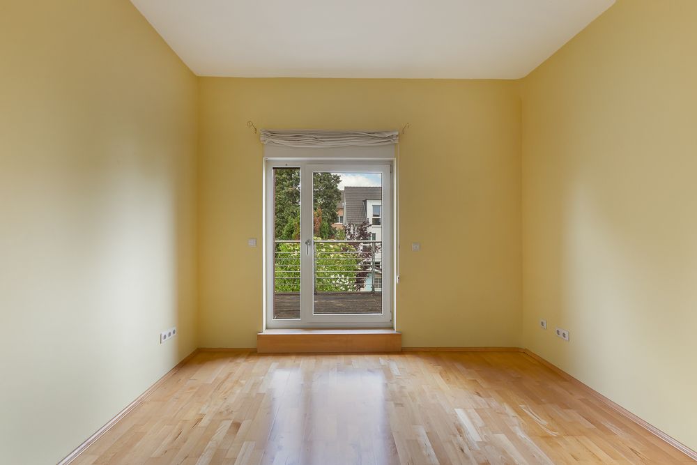 Leeres Zimmer mit gelben Wänden, Holzboden und Glastür zu einem Balkon.