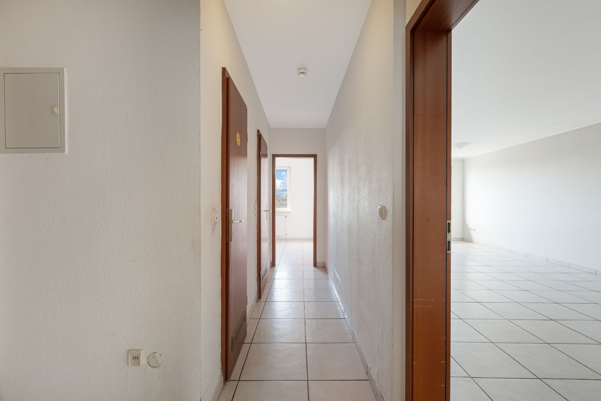 Heller Flur mit Fliesenboden, Holztüren und Zugang zu einem großen, leeren Zimmer.