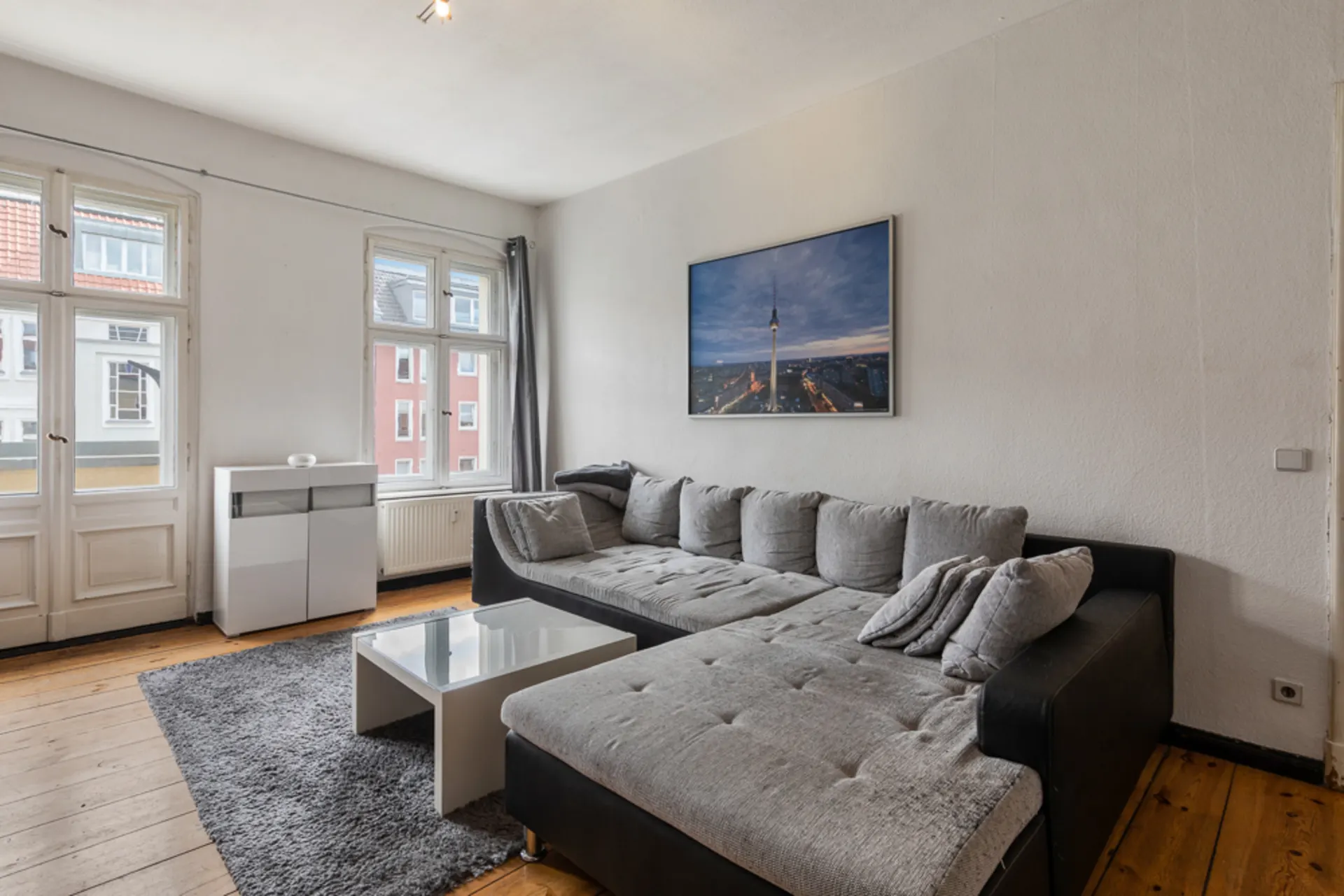 Helles Wohnzimmer mit grauem Ecksofa, Couchtisch und großem Bild an der Wand.