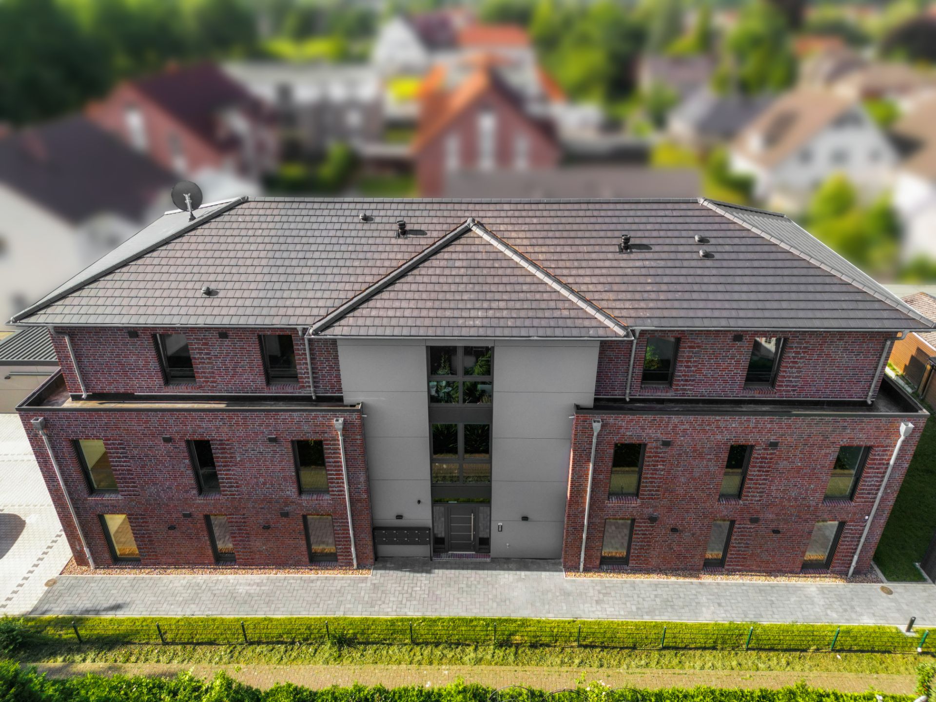 Modernes, zweistöckiges Mehrfamilienhaus mit Ziegelfassade und vielen Fenstern, von oben fotografiert.