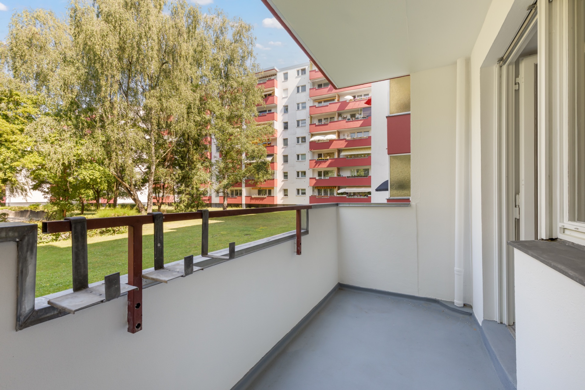 Balkon mit Blick auf grünen Innenhof und gegenüberliegendes Wohnhaus mit Bäumen.
