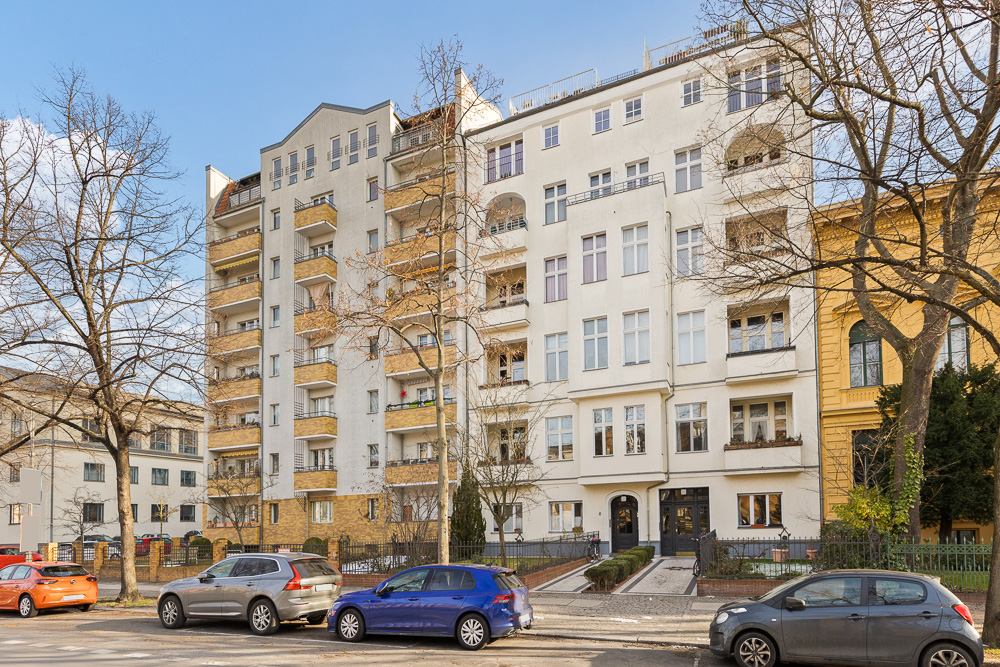 Mehrstöckiges Wohngebäude mit Balkonen und parkenden Autos davor.