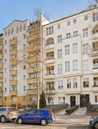 Mehrstöckiges Wohngebäude mit Balkonen und parkenden Autos davor.