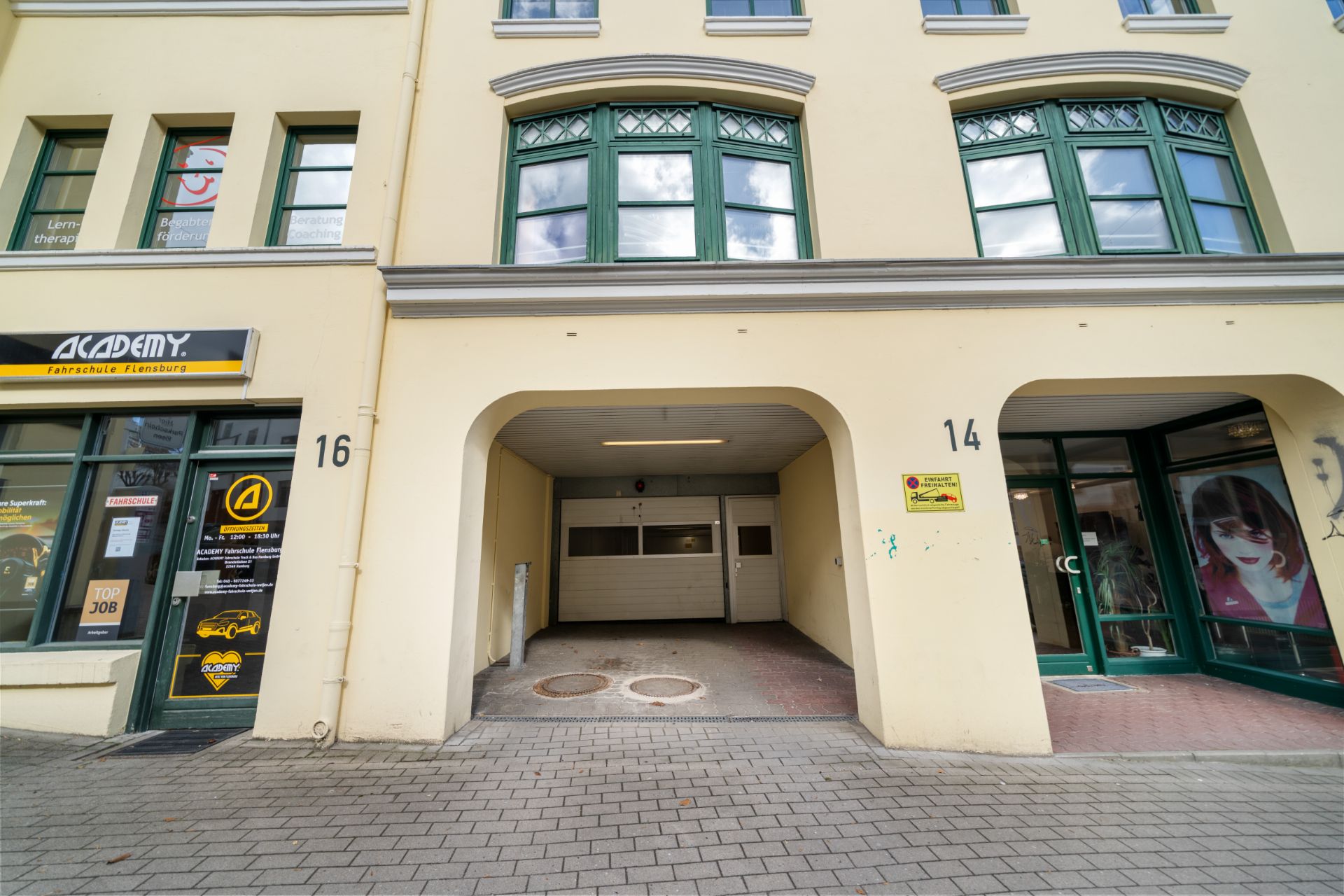 Eingang zu einer Tiefgarage in einem Wohngebäude mit grünen Fenstern und Hausnummern 14 und 16.