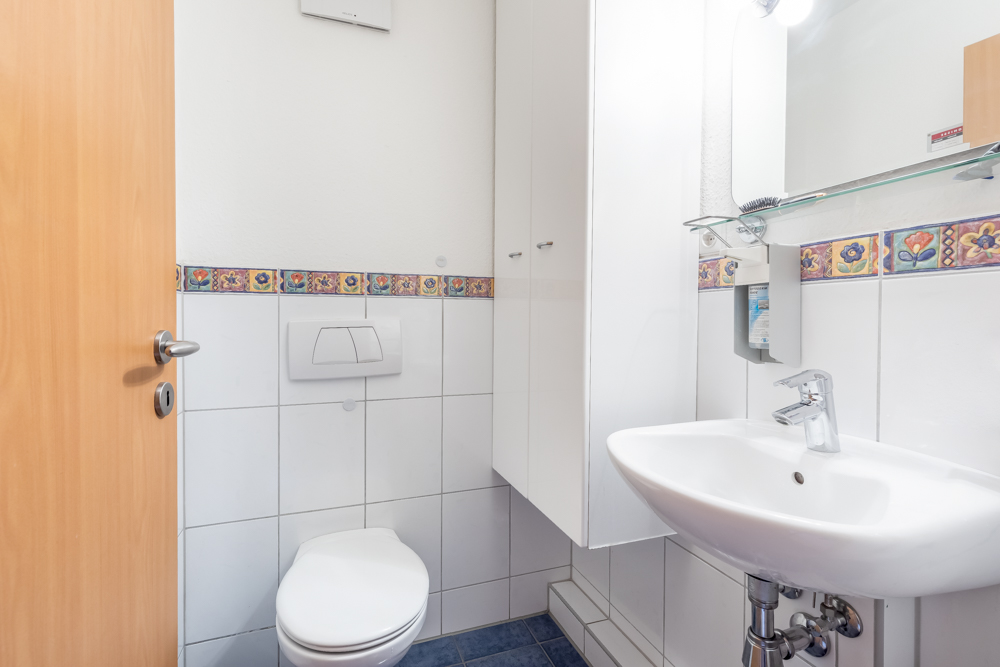 Kleines Badezimmer mit WC, Waschbecken und buntem Fliesenrand an der Wand.