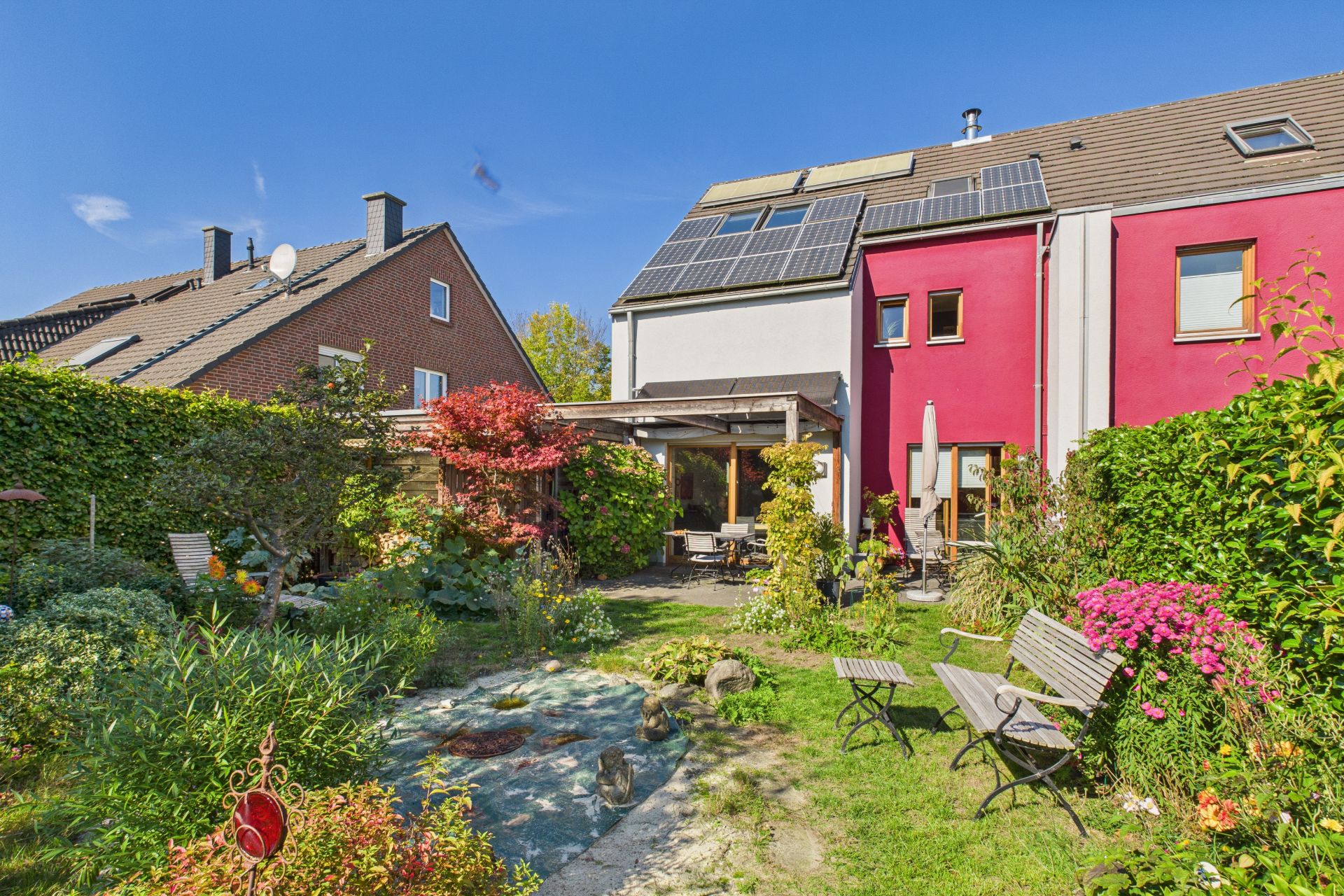 Garten mit Sitzmöbeln und Pflanzen hinter einem Reihenhaus mit Solarpanels auf dem Dach.