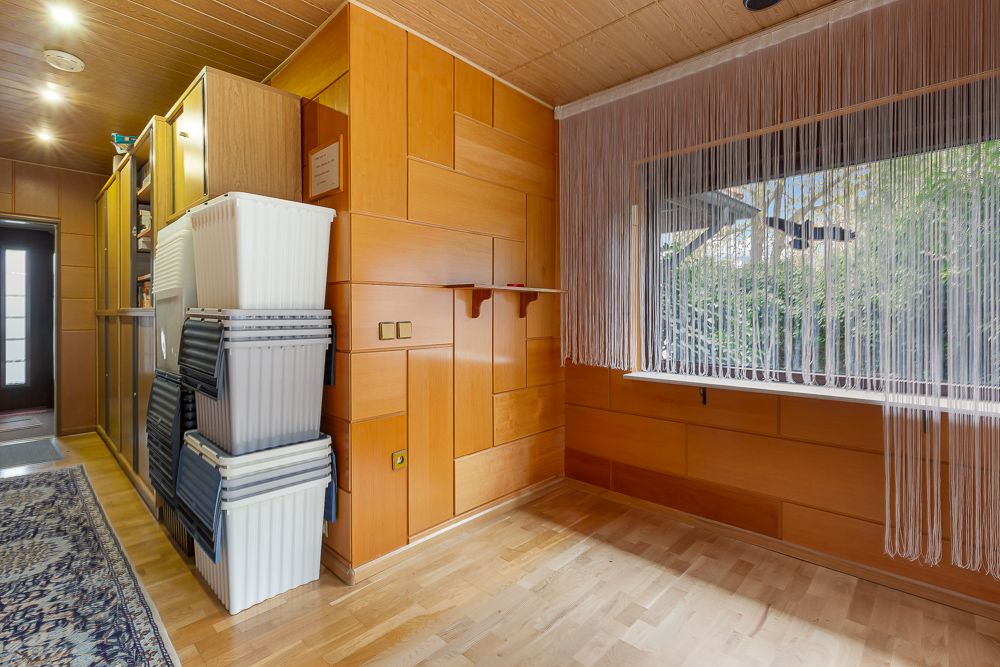 Raum mit Holzverkleidung, Regal, Plastikboxen, großem Fenster und Fadenvorhang.