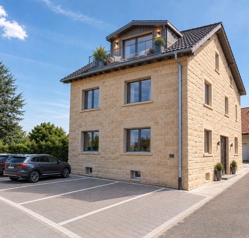 Modernes, mehrstöckiges Wohnhaus aus hellem Stein mit Balkon und angrenzendem Parkplatz.