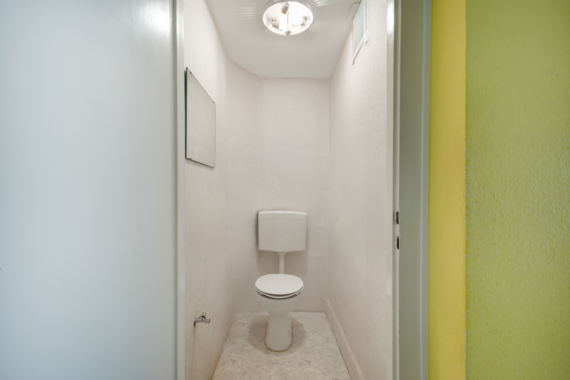 Kleines, schmales WC mit Toilette, Spiegel und Deckenlampe.