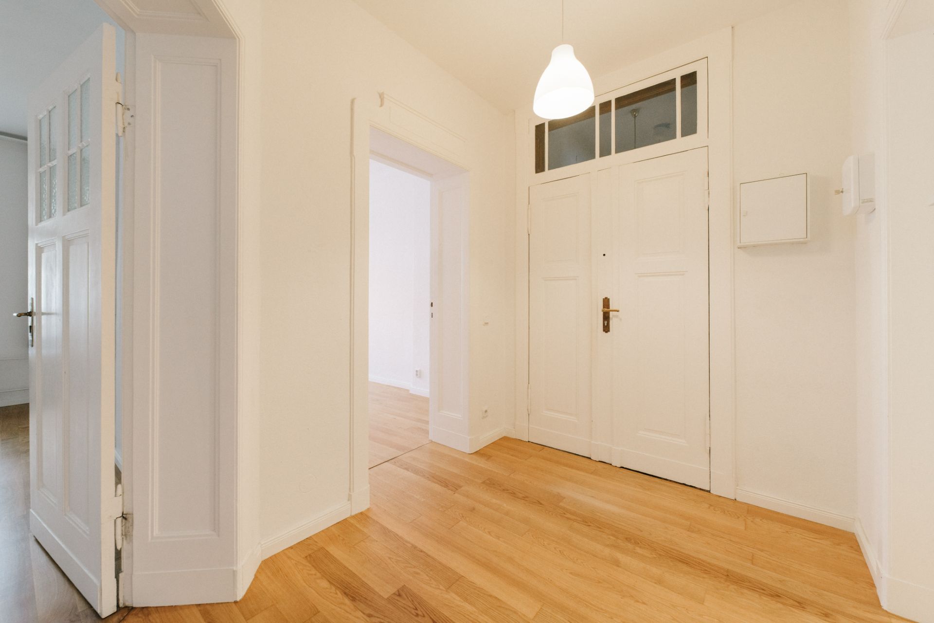 Heller Flur mit Holzboden, weißen Türen und einer Hängelampe.