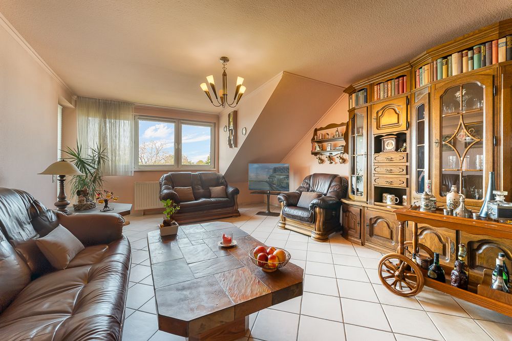 Wohnzimmer mit Ledersofas, Couchtisch, großem Fenster und Holzvitrine mit Büchern und Deko.