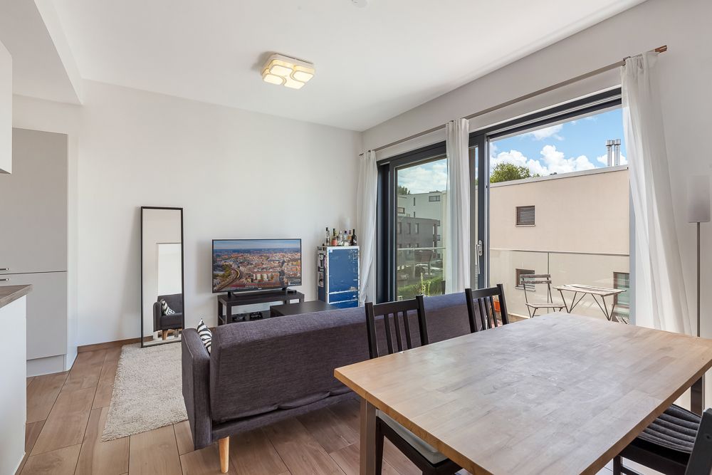Helles Wohnzimmer mit Esstisch, Sofa, Fernseher und großem Fenster zum Balkon.